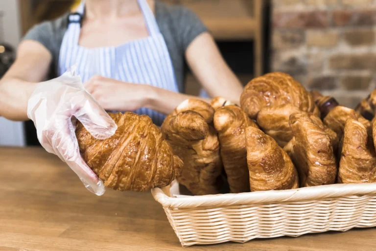 female-baker-s-hand-wearing-plastic-glove-taking-baked-croissant-from-basket (Web H)