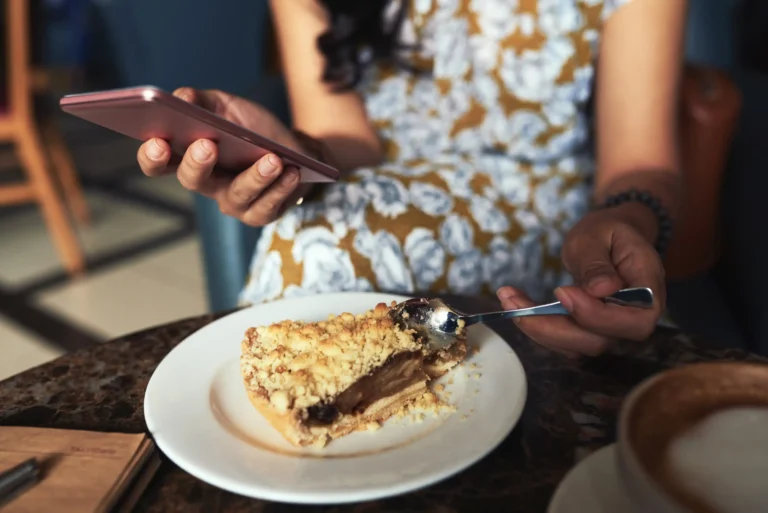 unrecognizable-young-woman-sitting-cafe-using-smartphone-eating-crumble-pie (Web H)